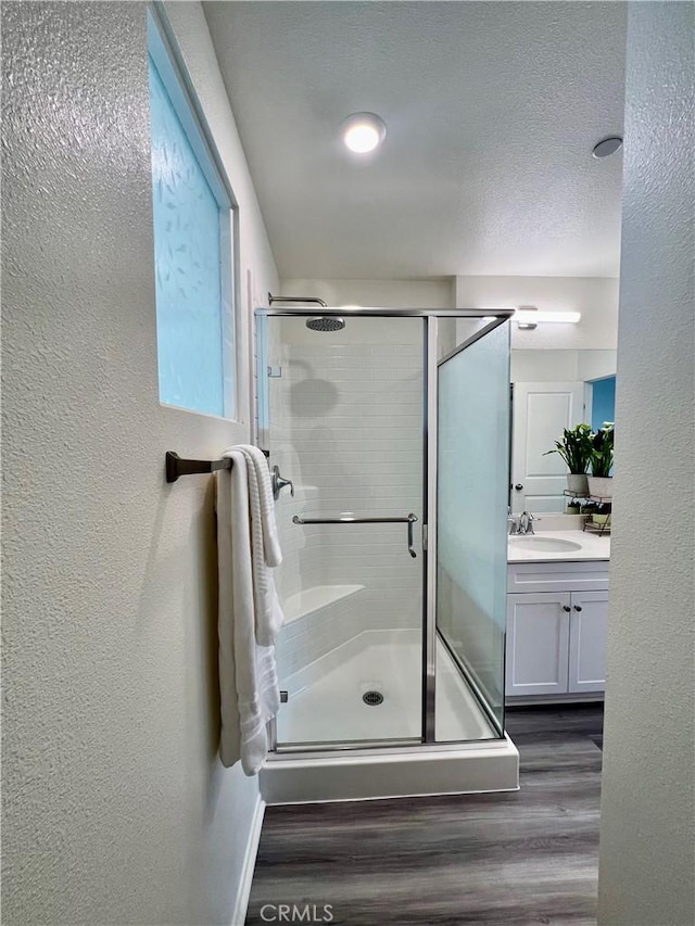 bathroom featuring a textured ceiling, a shower stall, vanity, wood finished floors, and a textured wall