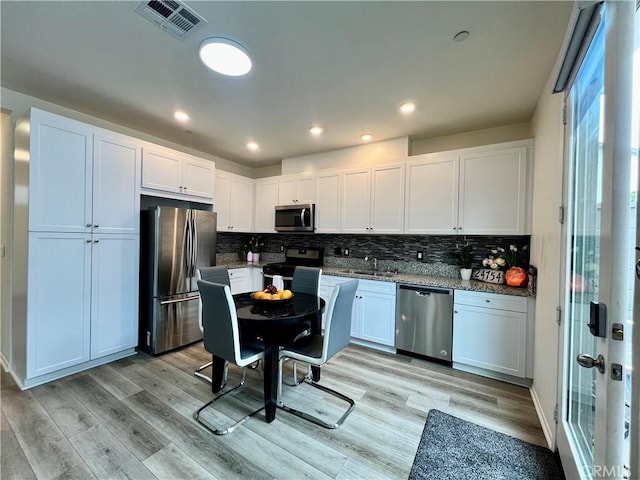 kitchen featuring visible vents, light wood finished floors, white cabinetry, decorative backsplash, and appliances with stainless steel finishes