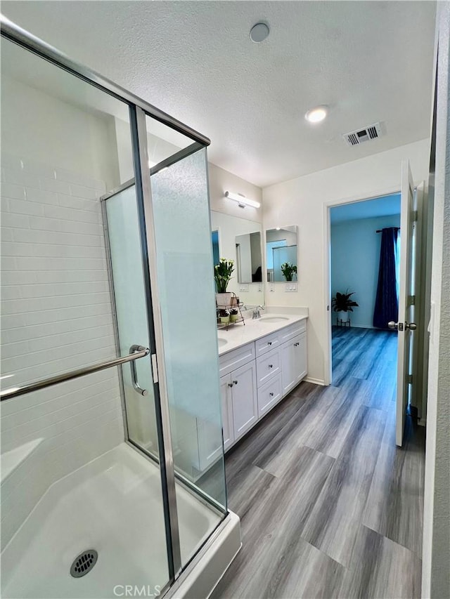 bathroom with a stall shower, a textured ceiling, visible vents, a sink, and double vanity