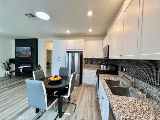 kitchen featuring light wood-style flooring, a sink, stainless steel appliances, white cabinets, and light stone countertops