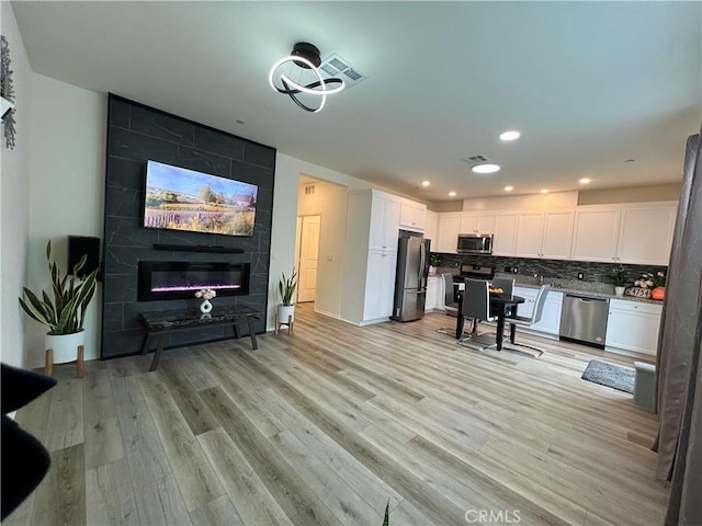 living room featuring recessed lighting, visible vents, a tiled fireplace, and light wood-style floors