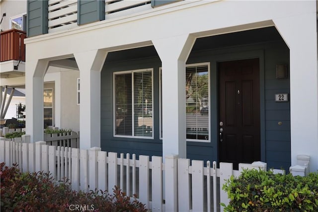 doorway to property featuring a porch, stucco siding, and fence