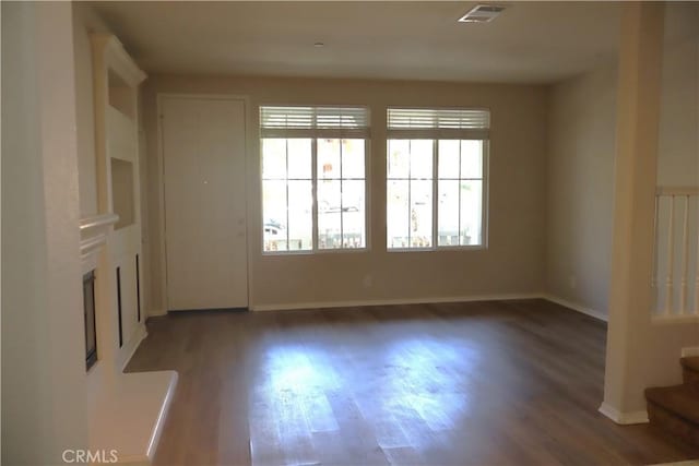 unfurnished room with wood finished floors, stairs, a fireplace with raised hearth, baseboards, and visible vents