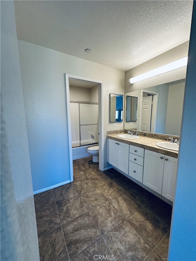 full bathroom featuring toilet, a textured ceiling, double vanity, and a sink