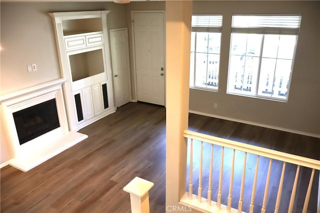 unfurnished living room featuring a fireplace with raised hearth, dark wood-style floors, and baseboards