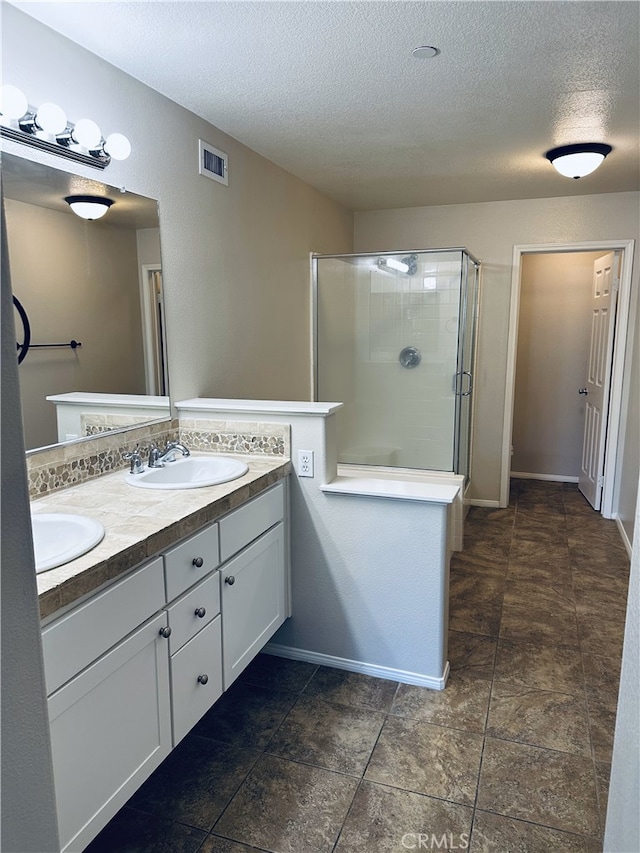 bathroom featuring a textured ceiling, a sink, a shower stall, and visible vents