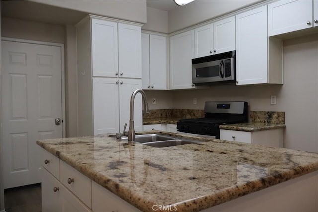 kitchen featuring appliances with stainless steel finishes, white cabinetry, light stone countertops, and a sink