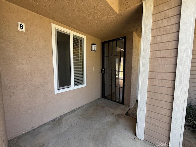 view of exterior entry featuring stucco siding and a patio