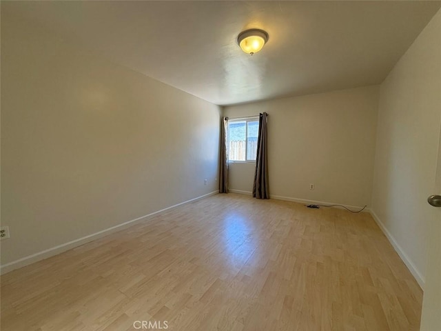 spare room with baseboards and light wood-style floors
