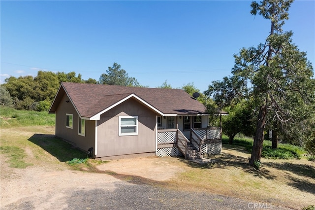 view of front facade featuring roof with shingles, a porch, and dirt driveway