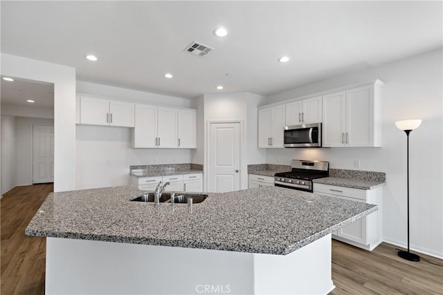 kitchen with appliances with stainless steel finishes, white cabinets, a sink, visible vents, and a center island with sink