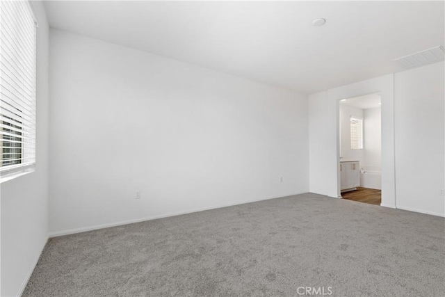 unfurnished bedroom with visible vents, connected bathroom, carpet flooring, and baseboards