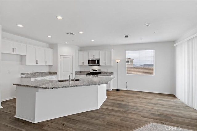 kitchen with a kitchen island with sink, a sink, stainless steel appliances, visible vents, and white cabinets