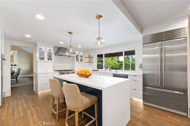 kitchen with white cabinets, light wood finished floors, modern cabinets, wall chimney range hood, and built in refrigerator