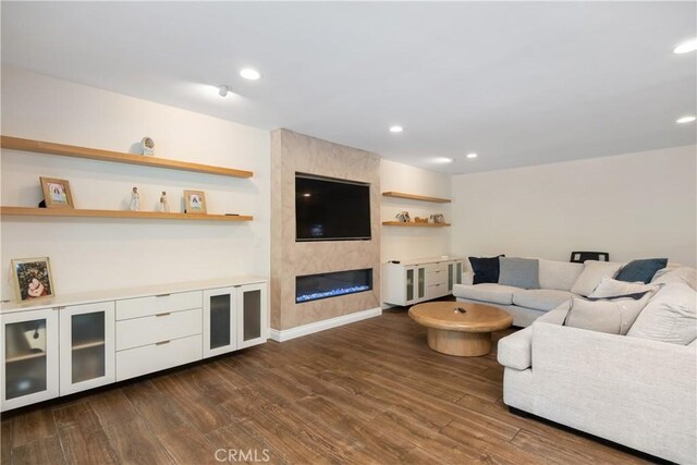 living area featuring baseboards, a large fireplace, dark wood-type flooring, and recessed lighting
