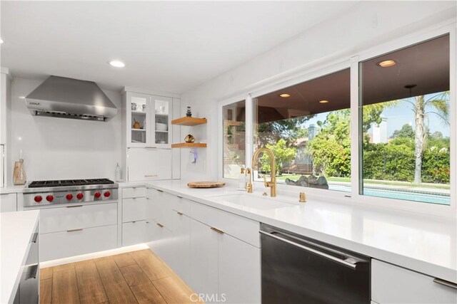 kitchen featuring white cabinets, stainless steel gas cooktop, a sink, wall chimney range hood, and dishwasher