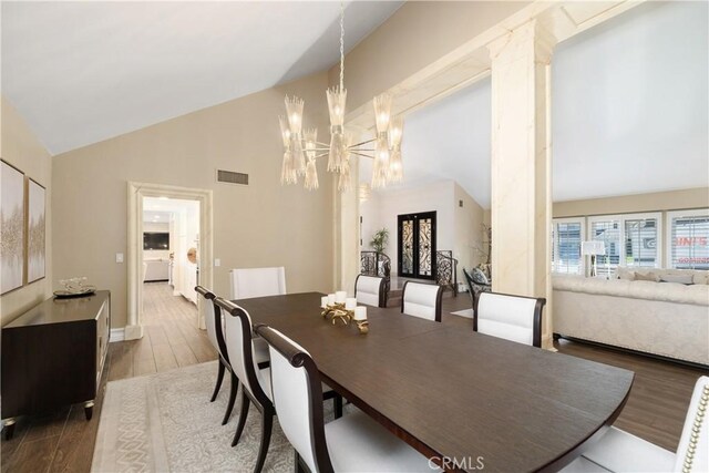 dining area featuring high vaulted ceiling, an inviting chandelier, wood finished floors, and visible vents