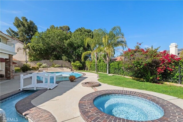 view of swimming pool featuring a patio area, a fenced in pool, a yard, and an in ground hot tub