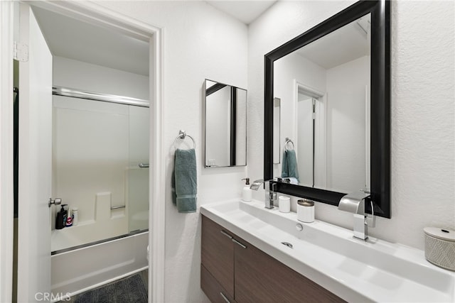 full bathroom featuring vanity, a textured wall, and combined bath / shower with glass door