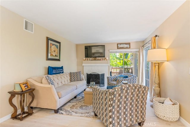 living area featuring a tiled fireplace, baseboards, wood finished floors, and visible vents