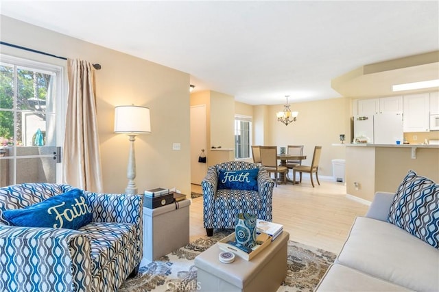 living area featuring baseboards, plenty of natural light, light wood finished floors, and a notable chandelier