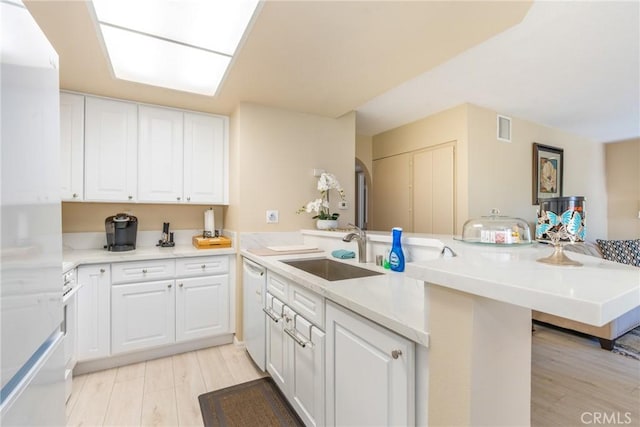 kitchen featuring white cabinets, a sink, light wood-style floors, white appliances, and a peninsula