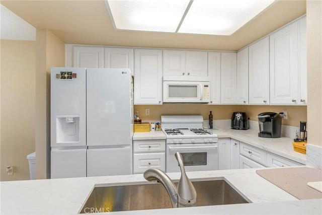 kitchen featuring white appliances, white cabinetry, light stone countertops, and a sink