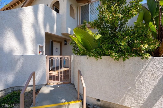 view of exterior entry with fence, a gate, stucco siding, and crawl space