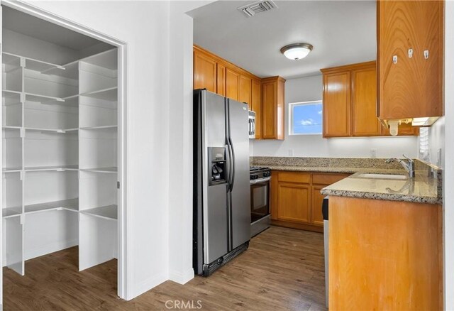 247 W 223rd St Unit D, Carson, CA 90745 - kitchen with stainless steel appliances, a sink, dark wood-style flooring, light stone countertops, and brown cabinets