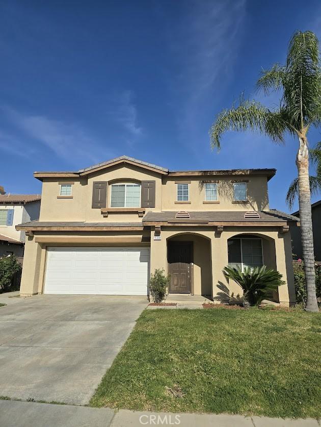 traditional-style home featuring stucco siding, an attached garage, driveway, and a front yard