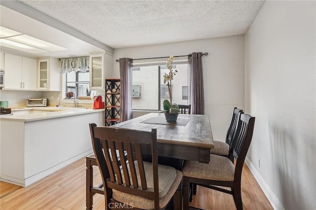 dining area featuring baseboards, light wood-style flooring, a textured ceiling, and a toaster