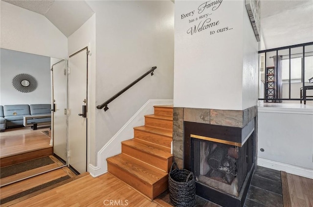 stairway featuring vaulted ceiling, wood finished floors, a tiled fireplace, and baseboards