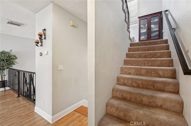 stairs featuring wood finished floors, visible vents, and baseboards