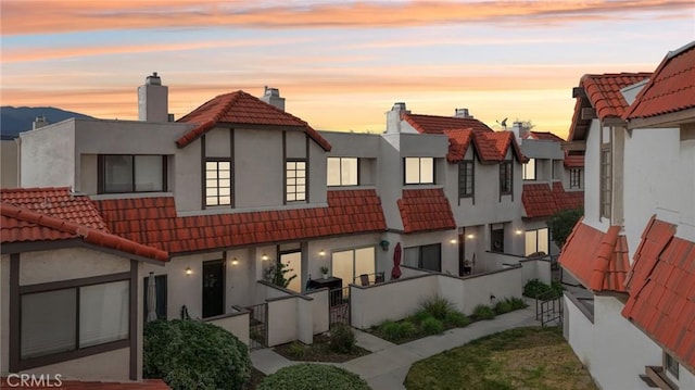 back of property at dusk featuring stucco siding, fence, a chimney, and a tiled roof