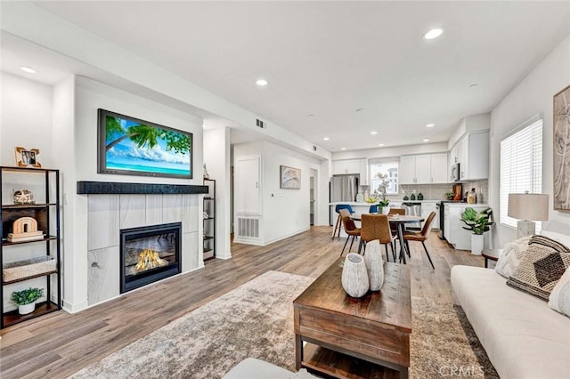living room with a fireplace, light wood-style flooring, and visible vents