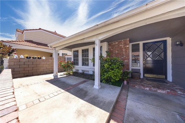 doorway to property featuring fence, covered porch, and brick siding