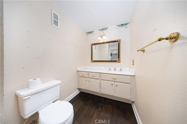 half bath featuring wood finished floors, baseboards, toilet, and vanity