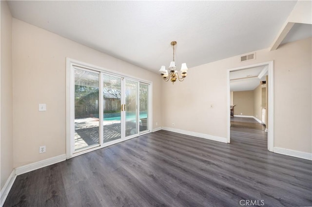 empty room with a chandelier, dark wood finished floors, and baseboards