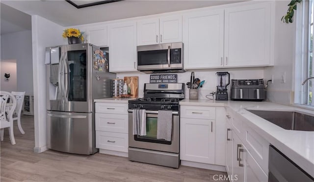 kitchen featuring white cabinets, light stone counters, stainless steel appliances, a sink, and light wood-type flooring