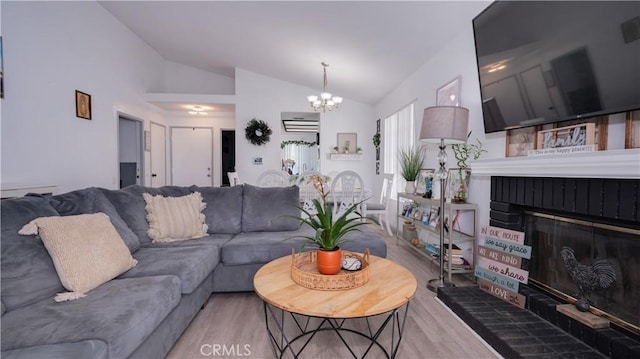 living area with vaulted ceiling, wood finished floors, a chandelier, and a brick fireplace