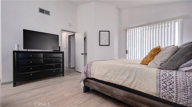 bedroom featuring a towering ceiling, visible vents, and light wood-style flooring