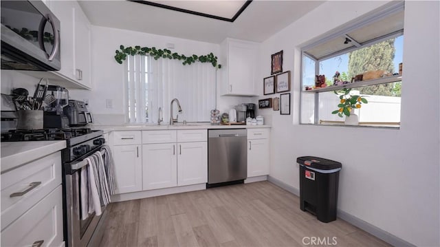 kitchen featuring a sink, light countertops, stainless steel appliances, light wood-style flooring, and white cabinets