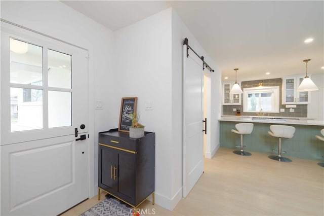 doorway to outside with a barn door, recessed lighting, a sink, light wood-style floors, and baseboards
