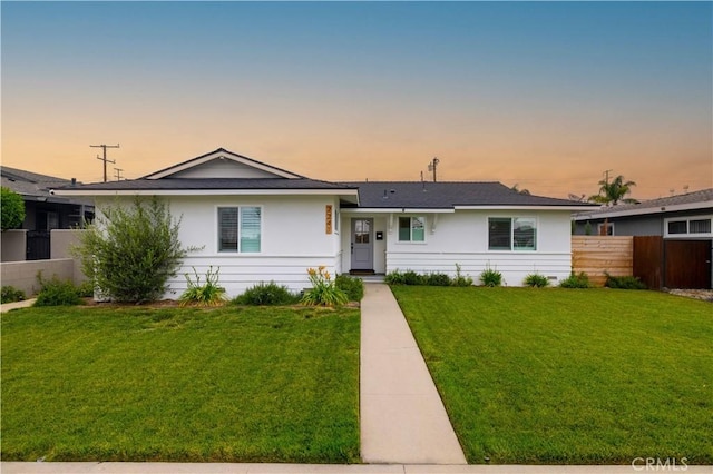 ranch-style house featuring a lawn and fence