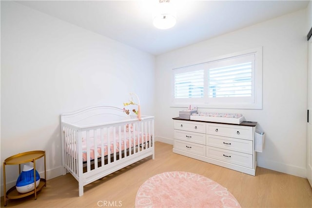 bedroom with a crib, baseboards, and light wood-style floors