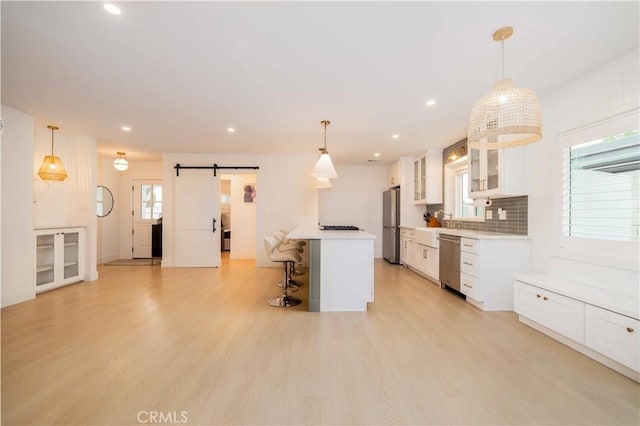 kitchen featuring a barn door, light wood-type flooring, a kitchen bar, white cabinets, and appliances with stainless steel finishes