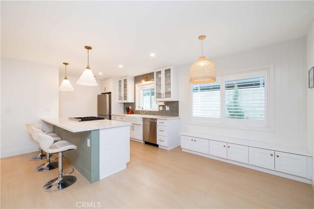 kitchen with white cabinets, backsplash, light wood-style floors, appliances with stainless steel finishes, and a breakfast bar area