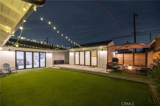 back of house at twilight with fence, a patio area, an outdoor fire pit, and a yard