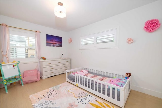 bedroom with a nursery area, baseboards, and wood finished floors
