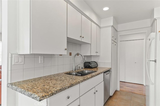 kitchen with white cabinets, stainless steel dishwasher, a sink, freestanding refrigerator, and decorative backsplash
